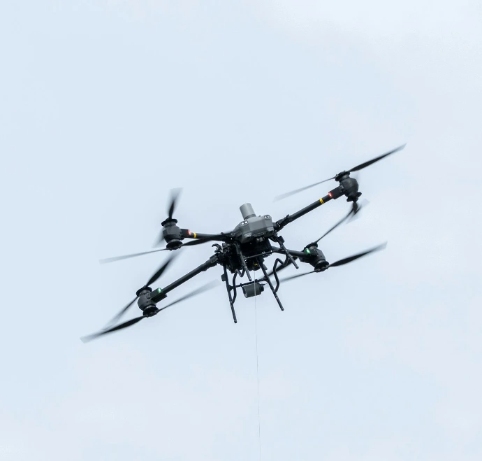 A drone flies against a cloudy sky.